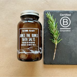 Image to show the new Packaging for Jones The Bones Bath Salts. An amber glass apothecary jar with aluminium lid, both recyclable. The label is illustrated with original illustration of The Clwydian Range