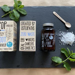 Amber glass jar and sprinkling of white Pop Fizzy Foot Reviver on a grey slate