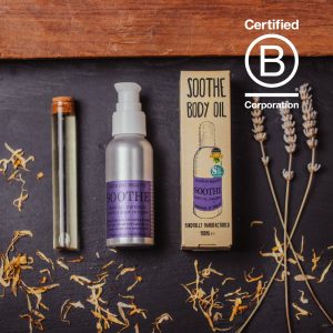 A black Slate showing a vial of pale yellow oil. A silver metal bottle of Soothe Oil with a purple label and a beige box with an illustration of a bottle of soothe oil. To the far right is a sprig of lavender, sprinkled over the bottom of the image are Calendula Petals