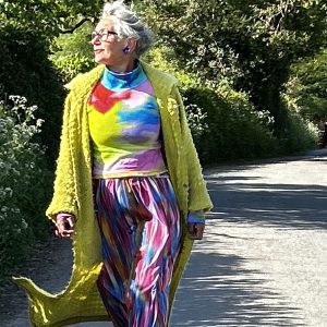 a photo to show a woman with grey hair walking wearing a beautiful rainbow dress and yello wcoat